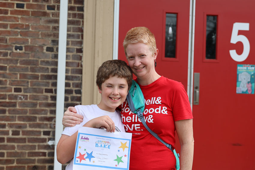 Mother with son outside school building holding B.I.K.E. award