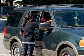 Staff member in parking lot handing device to family in their vehicle