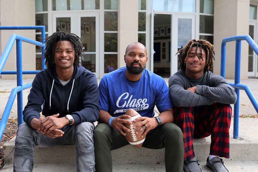 Coach Lovelace sitting on steps with two football players