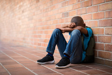 Student with backpack sitting with head down in arms