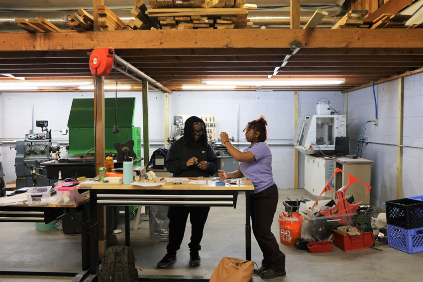 Two women at workbench with machining tools in background