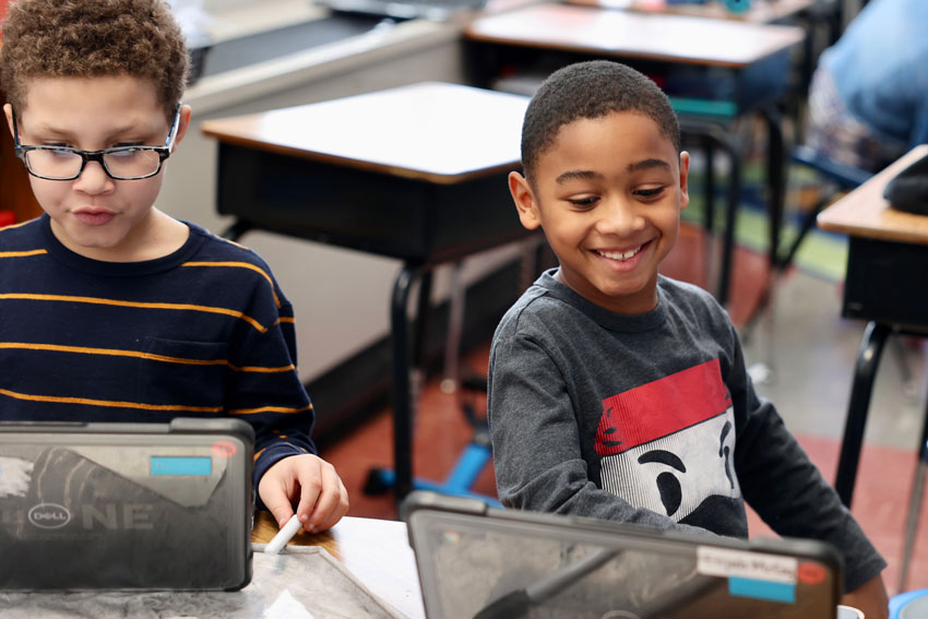 Two students working on laptops in classroom