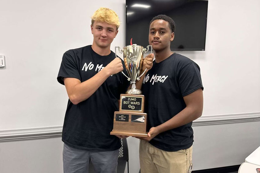 Two students in matching shirts holding trophy