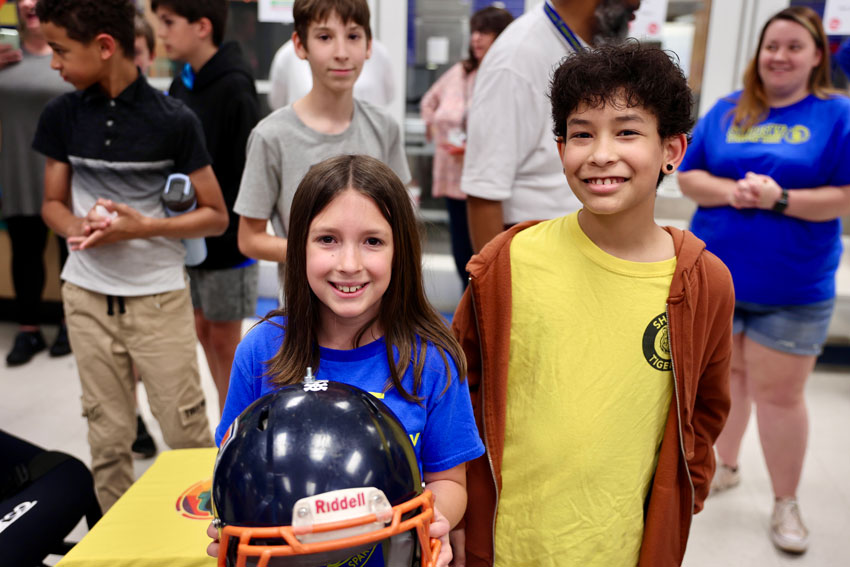 Two smiling students holding helmet from project